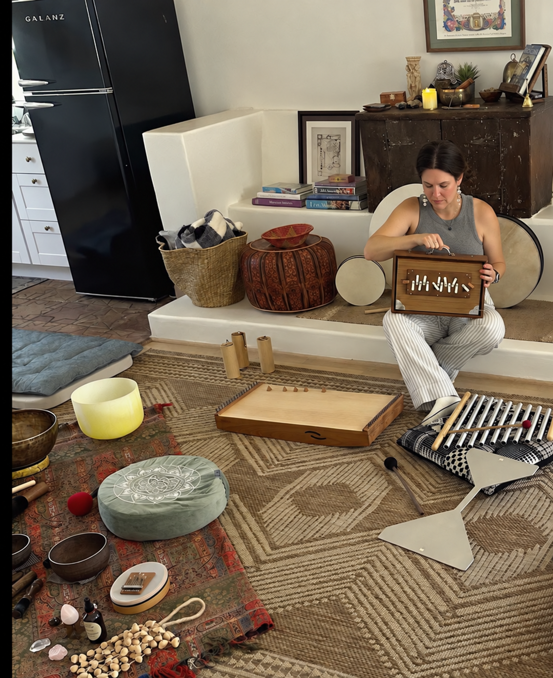 Kristen playing an instrument surrounded by singing bowls and percussion instruments